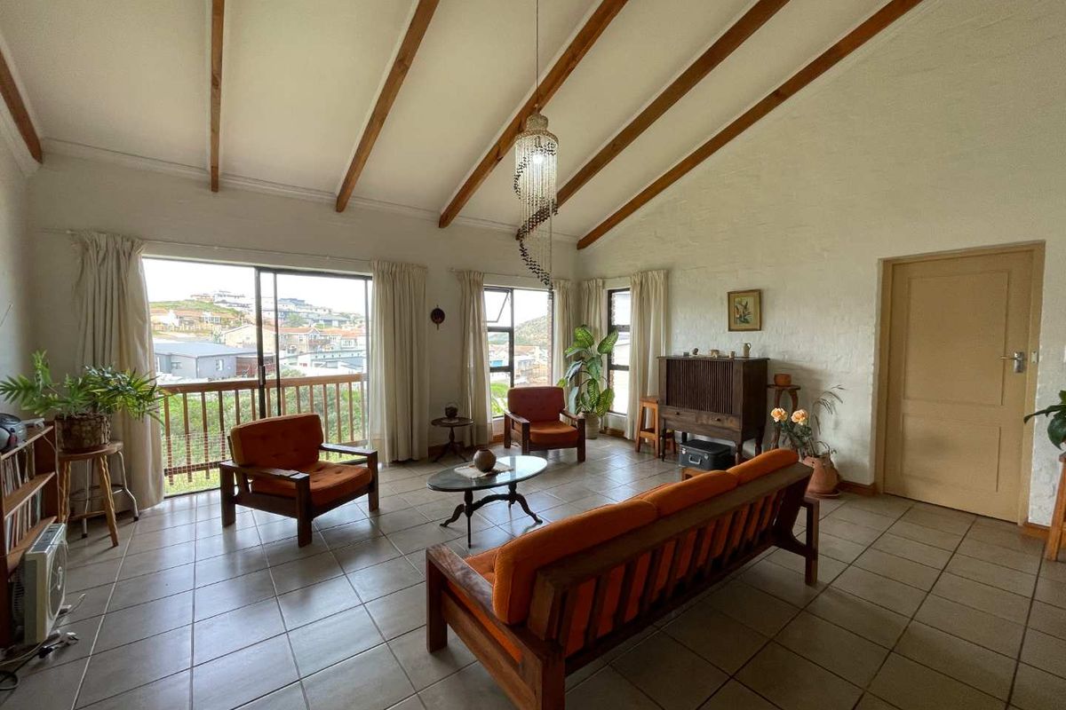 Spacious living room featuring high vaulted ceilings with exposed timber beams, tiled flooring, and large windows providing natural light and scenic views.