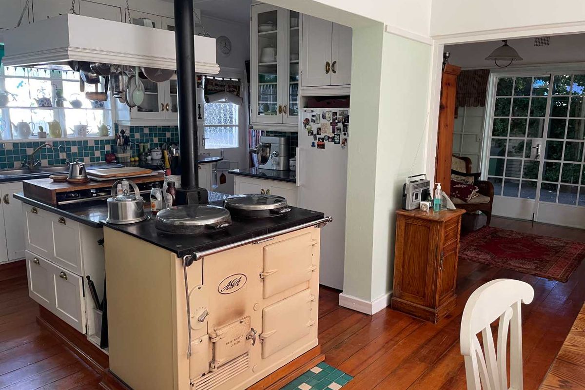 A character-filled kitchen featuring a classic AGA range cooker, white cabinetry, and timber flooring, opening into an adjacent living space with garden access.