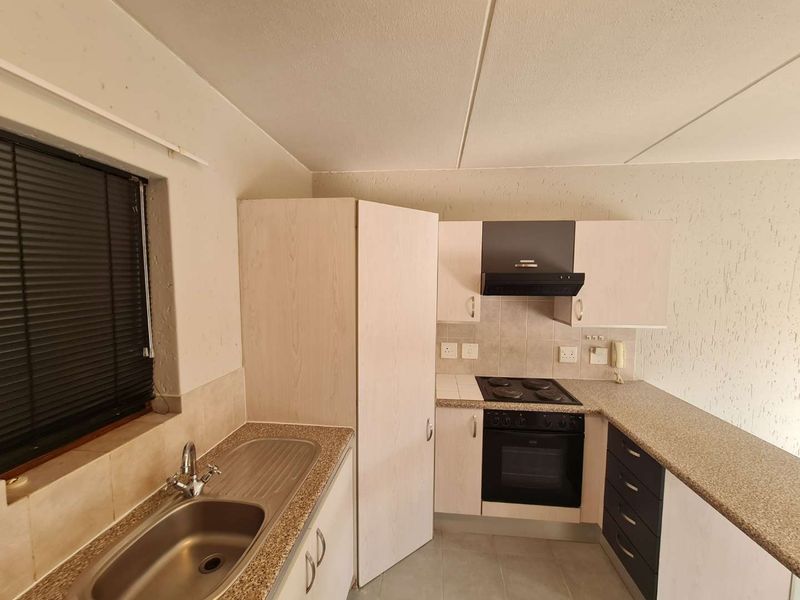 A functional kitchen featuring built-in cabinetry, a stainless steel sink, an electric hob with oven, and an extractor fan, offering a clean, blank canvas.