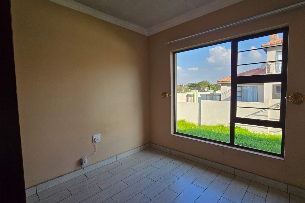 A bright, empty bedroom featuring tiled flooring, neutral wall tones, and a large window providing natural light and views of the surrounding property.