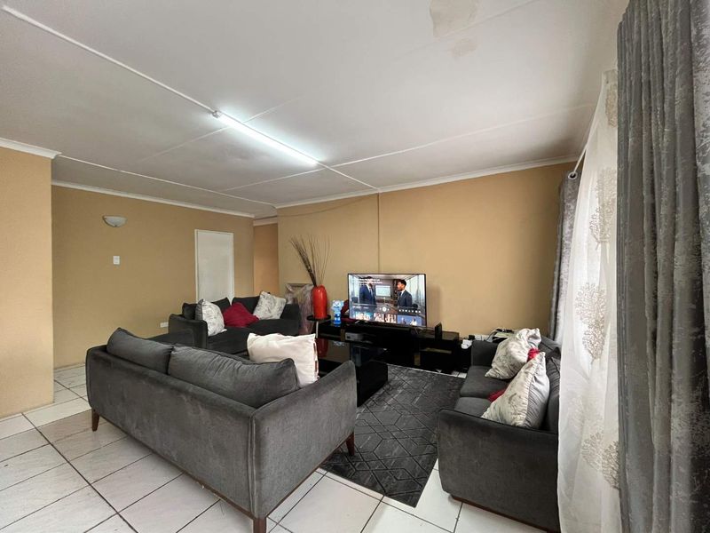 A living room featuring tiled flooring and a ceiling with visible panel joints and water staining, requiring cosmetic attention.