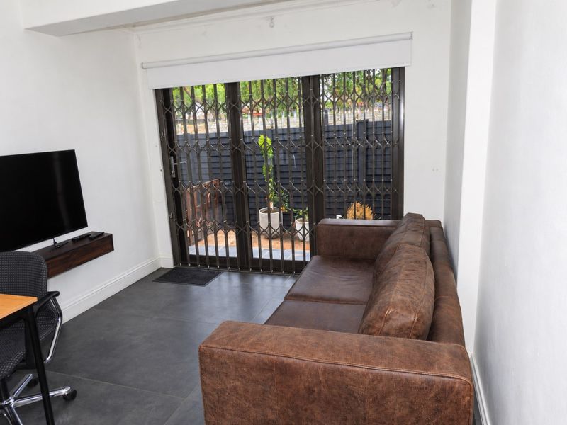 A living area featuring dark tiled flooring, a sliding door with a security gate, and a roller blind, providing access to the outdoor space.