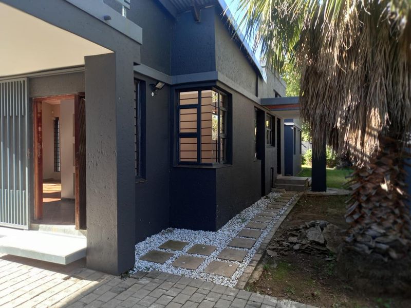 Rear exterior view of the house featuring dark painted walls, a paved walkway with pebble accents, and a corner window.
