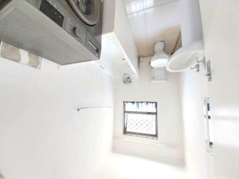 A functional bathroom featuring a bathtub, toilet, and pedestal basin, with tiled flooring and a window fitted with security bars.