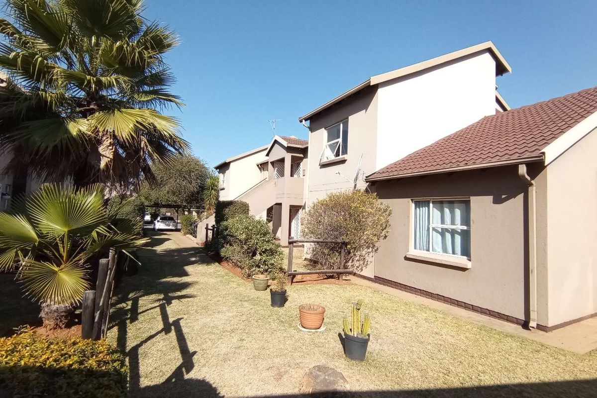 Rear view of the townhouse complex showing the garden area, plastered exterior walls, and tiled roofing.