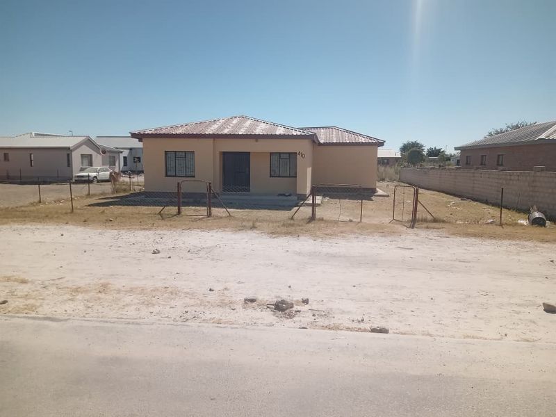 Front view of a single-story detached house featuring a metal roof, security bars on windows, and an unlandscaped yard with perimeter fencing.