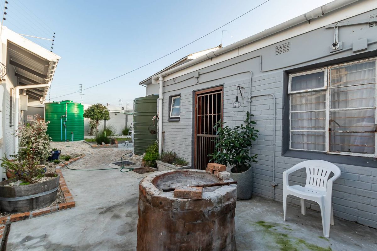 Rear exterior area featuring concrete paving, water storage tanks, and a fixed brick braai structure against a painted masonry wall.