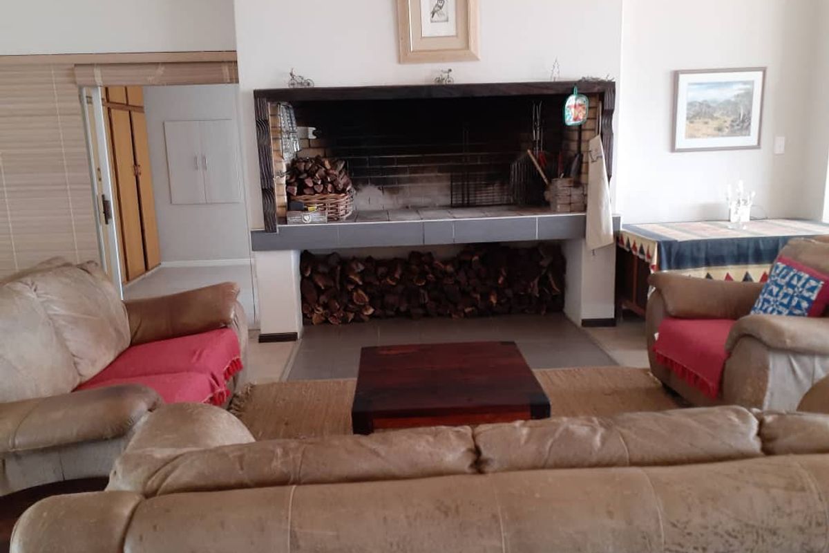 A cozy living room featuring a large built-in indoor braai fireplace with brick detailing and tiled hearth, creating a warm focal point for the space.
