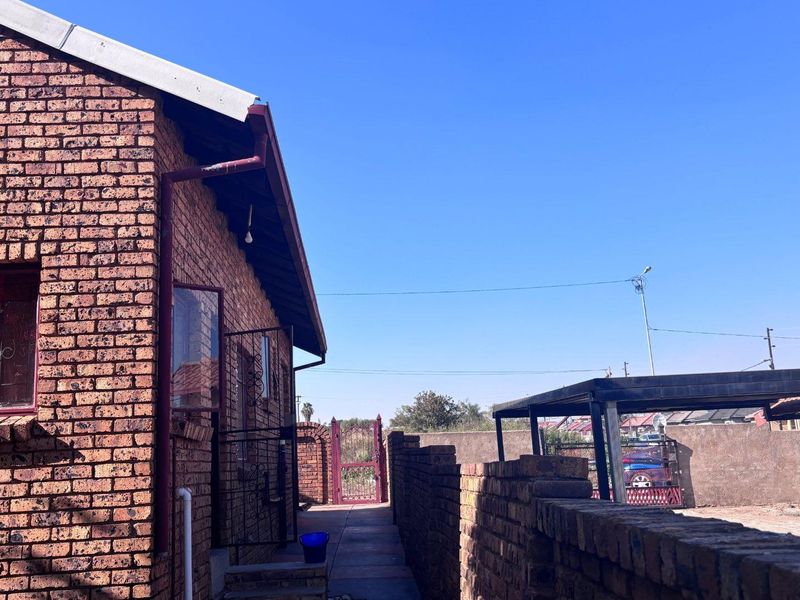 Side view of the property featuring exposed brick exterior, metal security gate, and a covered carport structure.
