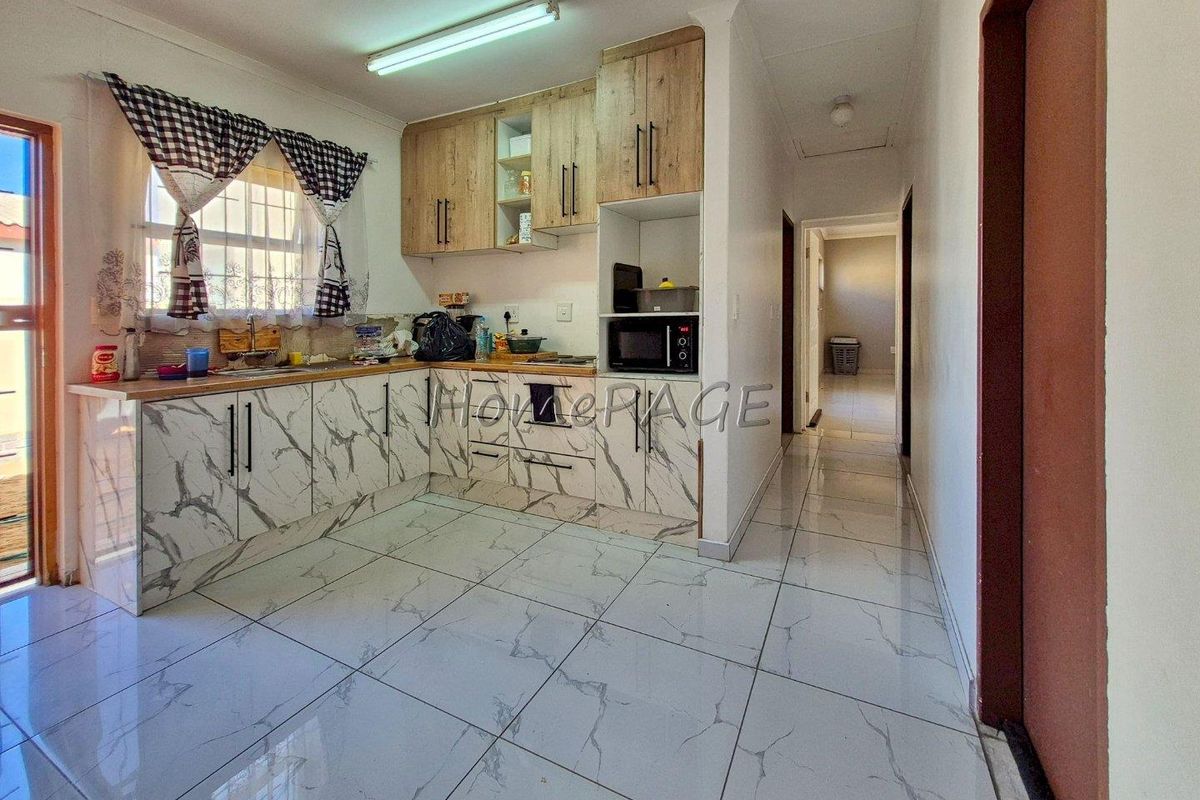 A functional kitchen featuring marble-look cabinetry, tiled flooring, and built-in storage, leading into a hallway area.