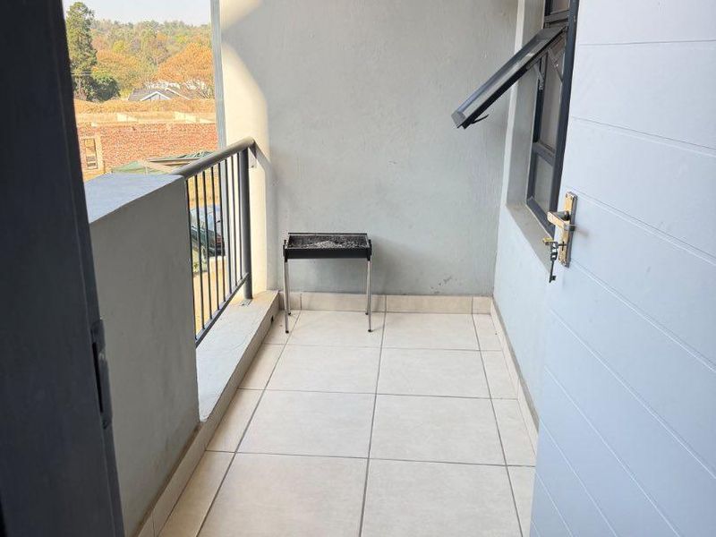 A clean, tiled balcony featuring a metal balustrade and an external door, offering an open-air space with a view.