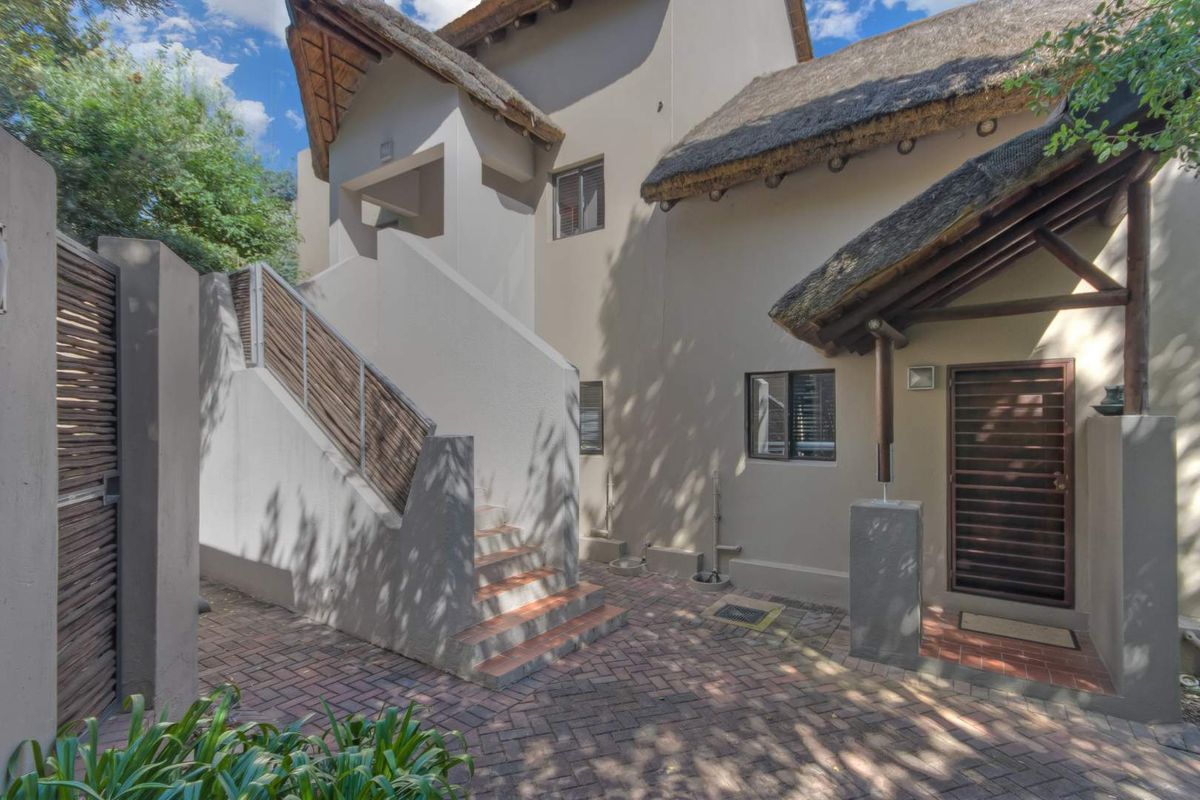 Exterior view of an apartment entrance featuring a thatched roof, paved courtyard, and external staircase leading to an upper level.