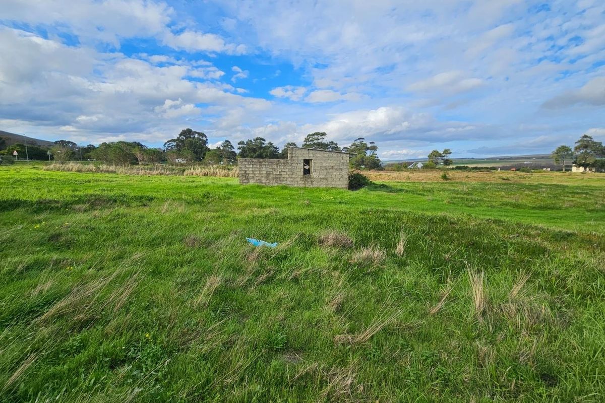 A view of a small, unfinished concrete block structure situated on a large, open grassy farm plot.