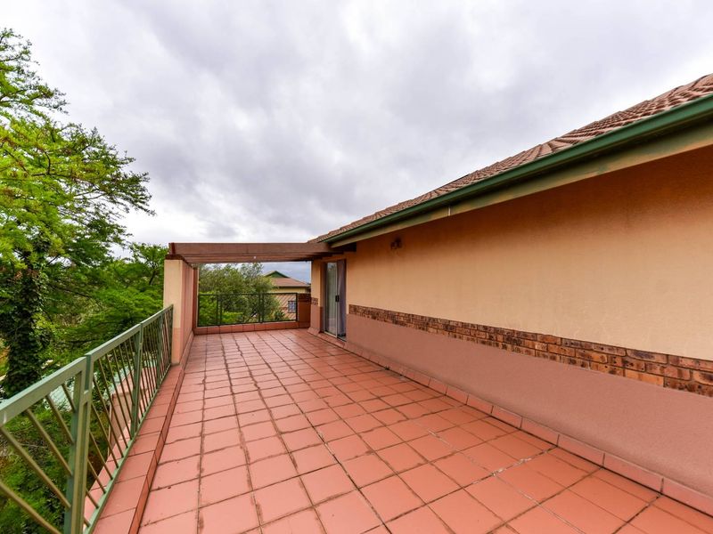 Spacious outdoor balcony featuring terracotta tiled flooring, a metal balustrade, and a timber pergola, providing an open-air space accessible via sliding glass doors.