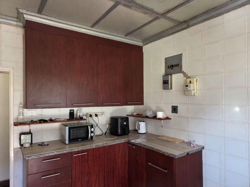 A dated kitchen featuring dark wood cabinetry, laminate countertops, and full-height wall tiling, offering significant potential for a modern renovation.
