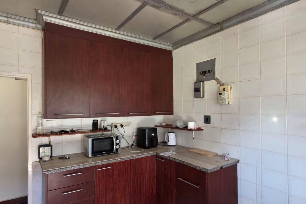 A dated kitchen featuring dark wood cabinetry, laminate countertops, and full-height wall tiling, offering significant potential for a modern renovation.