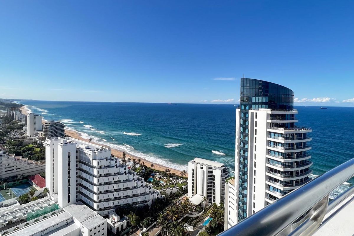 Stunning elevated coastal view overlooking the ocean, beach, and surrounding high-rise apartment buildings from a private balcony.