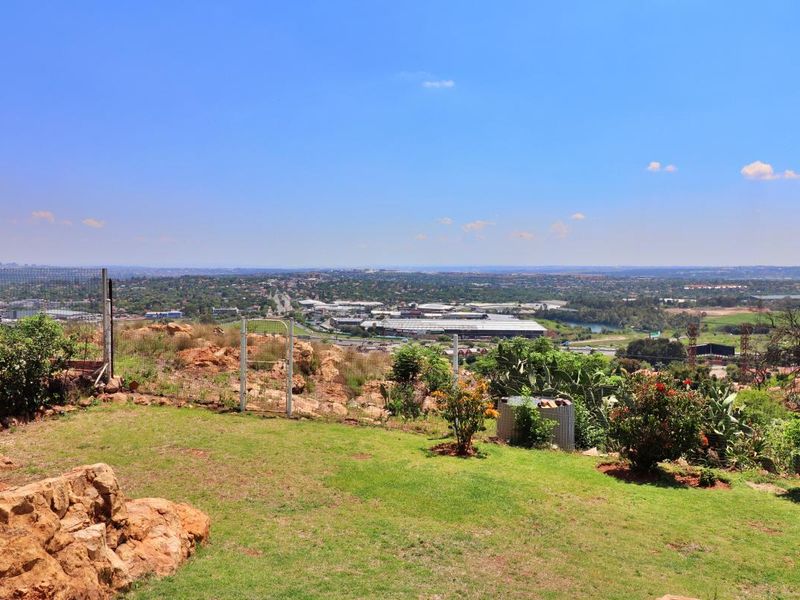 Elevated outdoor area featuring natural rock formations, manicured lawn, and expansive panoramic views over the surrounding landscape and urban infrastructure.