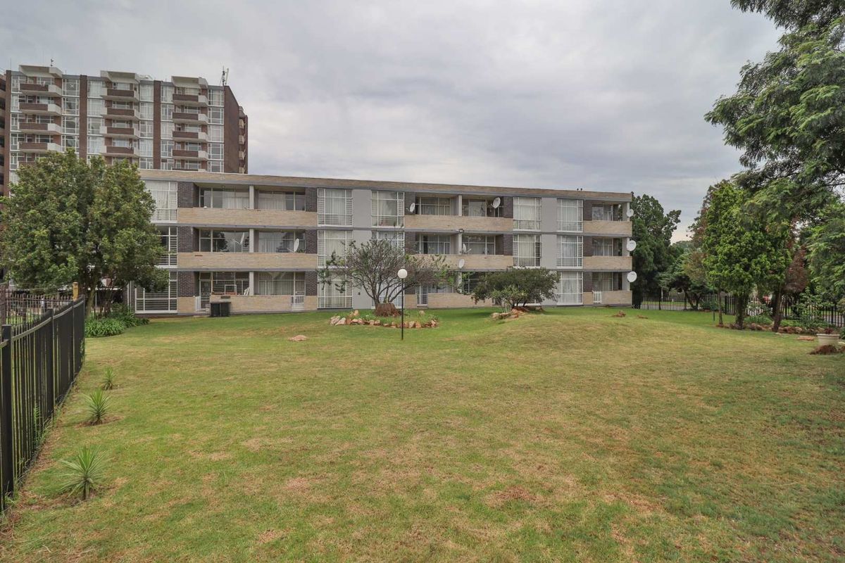 Rear view of a multi-story apartment complex featuring brick facade, sliding glass balcony doors, and a shared communal garden area.
