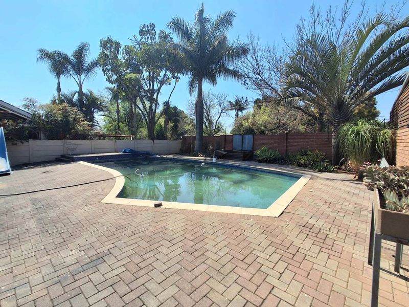 Outdoor pool area featuring a swimming pool surrounded by brick paving and enclosed by brick and precast concrete boundary walls.