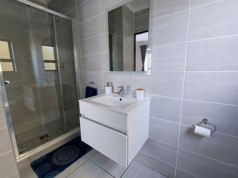 Modern bathroom featuring a glass shower enclosure, wall-mounted vanity with basin, and neutral grey ceramic tiling throughout.