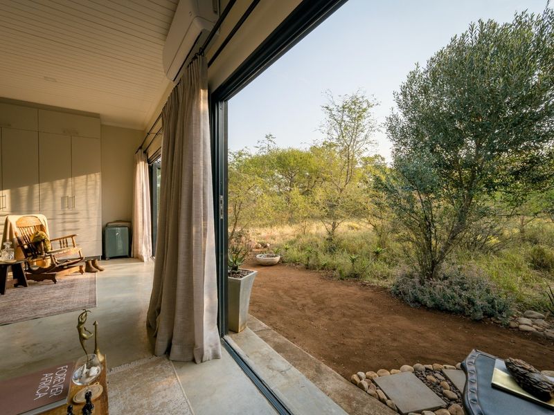 Bright living area featuring polished concrete floors, built-in cabinetry, and large sliding glass doors that open directly onto a natural bushveld garden.