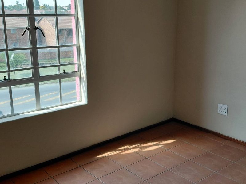 An empty bedroom featuring tiled flooring, a window with security bars, and a neutral wall finish, offering a blank canvas for personalization.