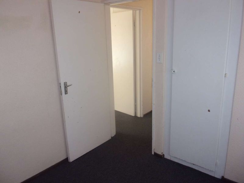 A functional hallway featuring carpeted flooring, internal doors, and a built-in cupboard, showing signs of wear and tear on the walls and door finishes.