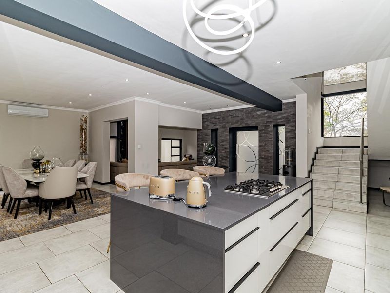 Modern open-plan living area featuring a sleek kitchen island with gas cooktop, stone countertops, tiled flooring, and a contemporary staircase.