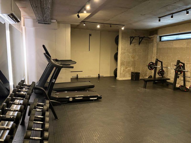 A functional home gym featuring industrial-style exposed concrete ceilings, track lighting, and durable rubber flooring, equipped with wall-mounted fitness infrastructure.