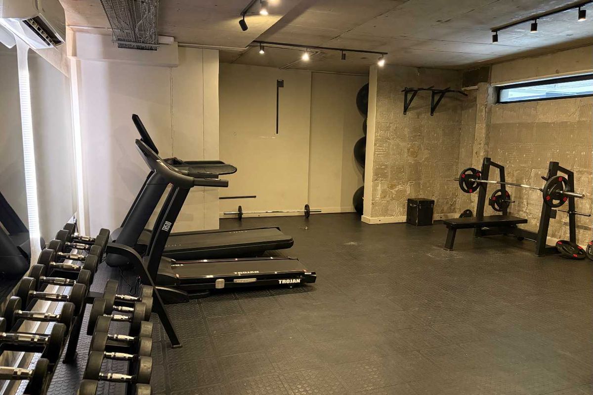 A functional home gym featuring industrial-style exposed concrete ceilings, track lighting, and durable rubber flooring, equipped with wall-mounted fitness infrastructure.