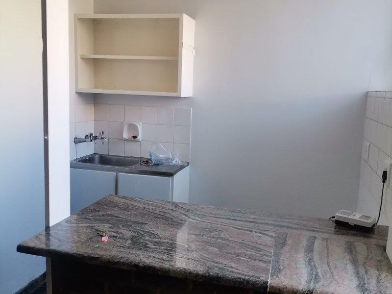 A compact kitchen area featuring a granite-topped breakfast bar with a brick base, stainless steel sink, and wall-mounted shelving.
