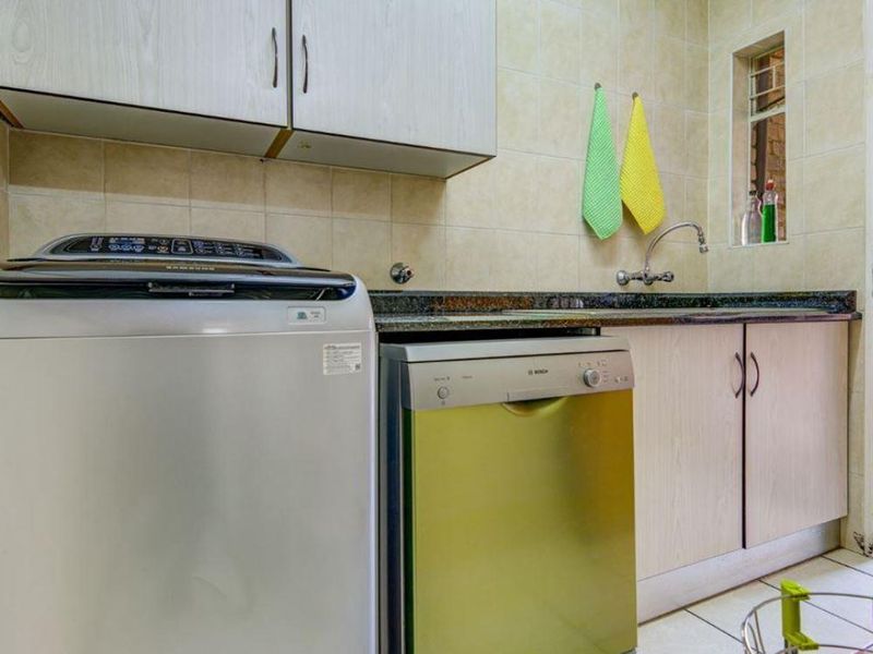 Functional laundry area featuring built-in cabinetry, granite countertops, a stainless steel sink, and tiled finishes.