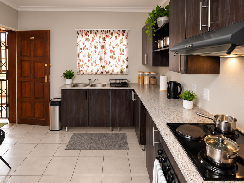 A functional kitchen featuring dark wood cabinetry, laminate countertops, a stainless steel double sink, and a built-in electric hob with an extractor fan.