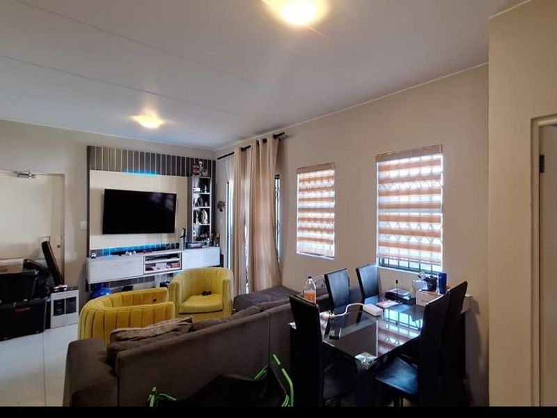 Open-plan living and dining area featuring tiled flooring, built-in media cabinetry, and dual windows with fitted roller blinds.