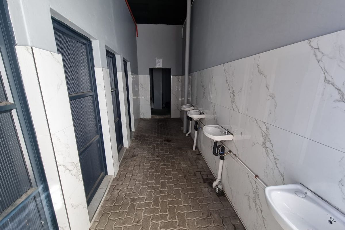A functional washroom area featuring multiple wall-mounted ceramic basins, marble-effect tiled walls, and paved flooring, suitable for commercial or retail use.