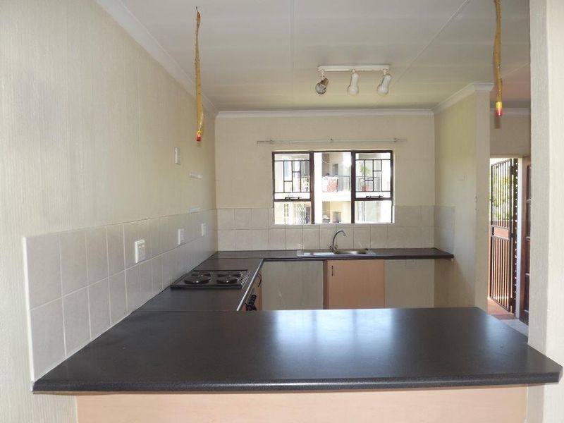 A functional, empty kitchen featuring dark laminate countertops, built-in cabinetry, a stainless steel sink, and a built-in hob with tiled backsplash.