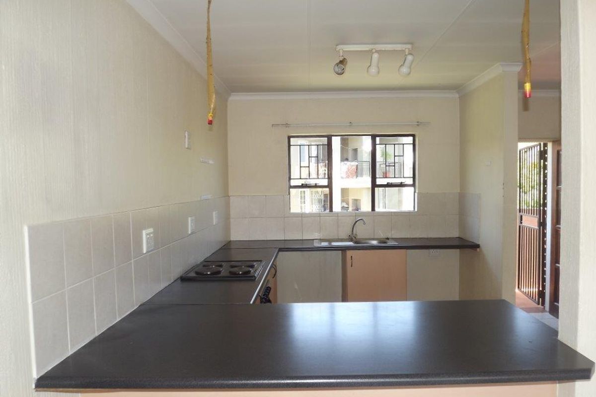 A functional, empty kitchen featuring dark laminate countertops, built-in cabinetry, a stainless steel sink, and a built-in hob with tiled backsplash.