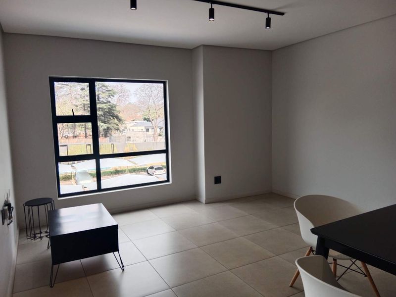 A bright and spacious living area featuring large windows, modern track lighting, and neutral tiled flooring, offering a clean and contemporary aesthetic.