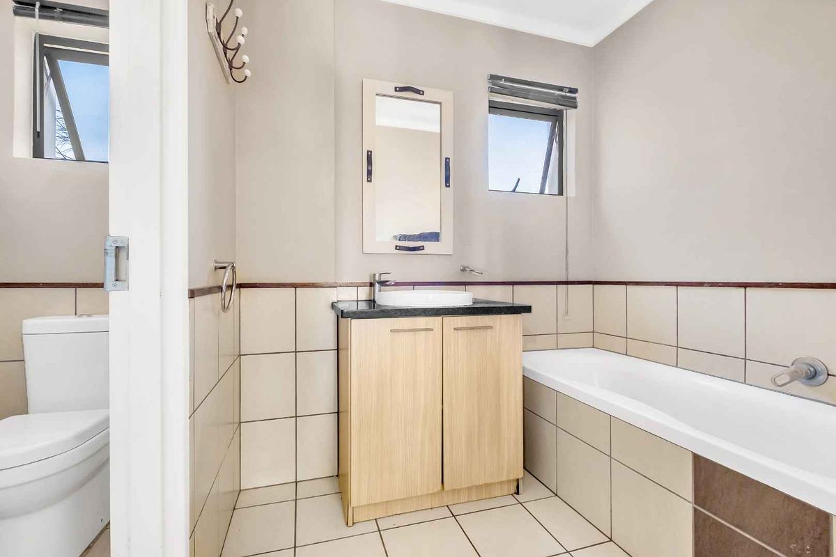 A functional bathroom featuring a vanity with a vessel sink, a bathtub, and a separate toilet area with neutral tiling.