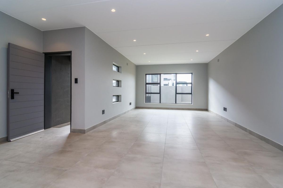 A spacious, modern, and empty living area featuring neutral tiled flooring, recessed ceiling lighting, and large aluminum-framed windows.