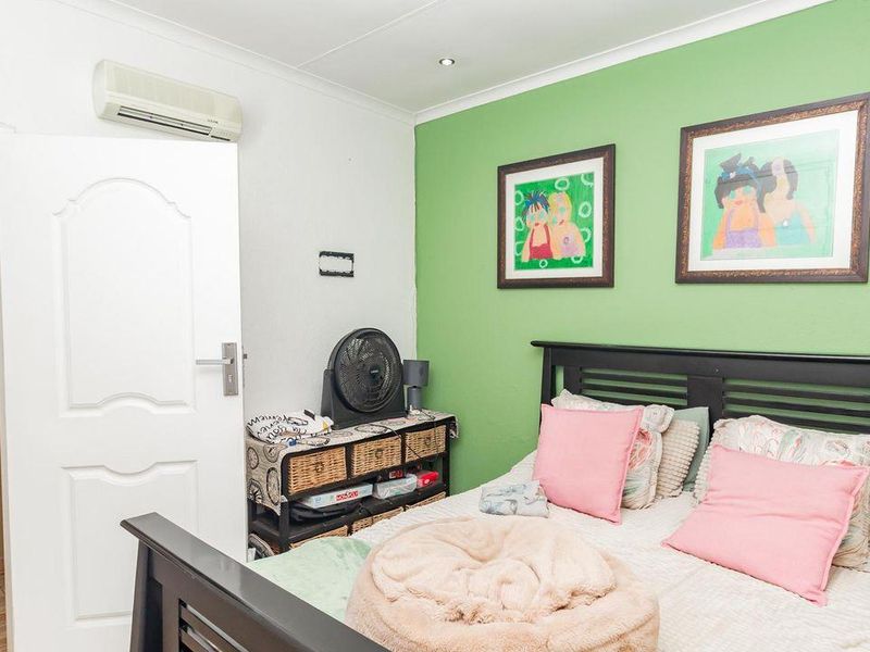 A bedroom featuring laminate flooring, recessed ceiling lighting, and a wall-mounted air conditioning unit, with a green accent wall.