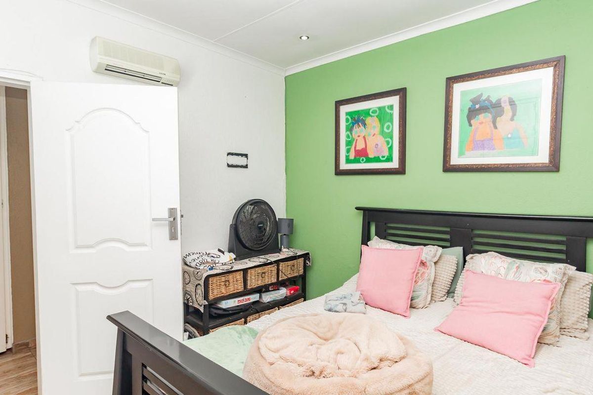 A bedroom featuring laminate flooring, recessed ceiling lighting, and a wall-mounted air conditioning unit, with a green accent wall.