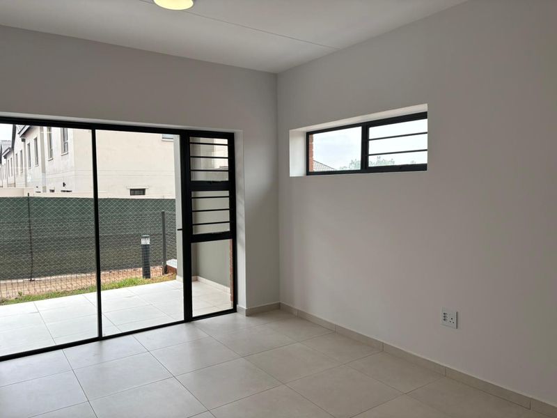 A bright, empty living area featuring neutral tiled flooring, a large sliding glass door leading to a patio, and modern window finishes.