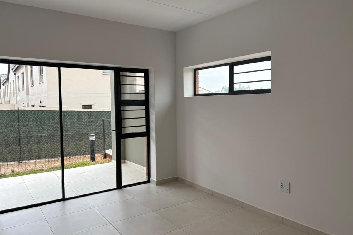 A bright, empty living area featuring neutral tiled flooring, a large sliding glass door leading to a patio, and modern window finishes.