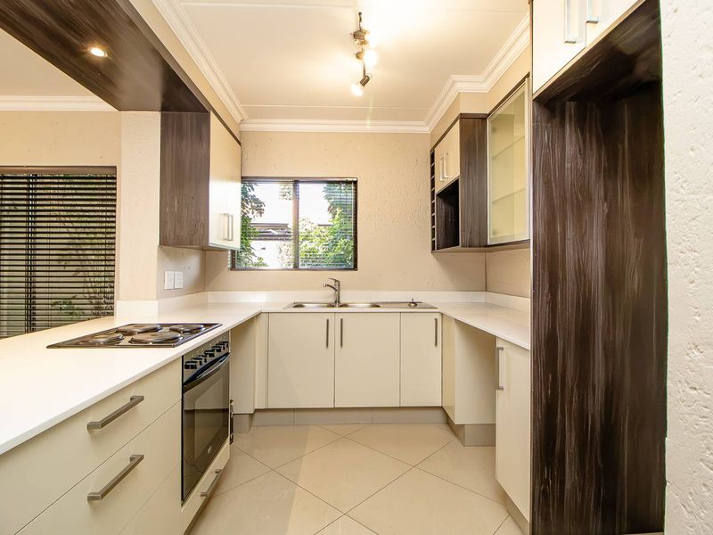 Modern kitchen featuring sleek built-in cabinetry, stone countertops, an electric hob with oven, and tiled flooring in a well-lit, functional layout.