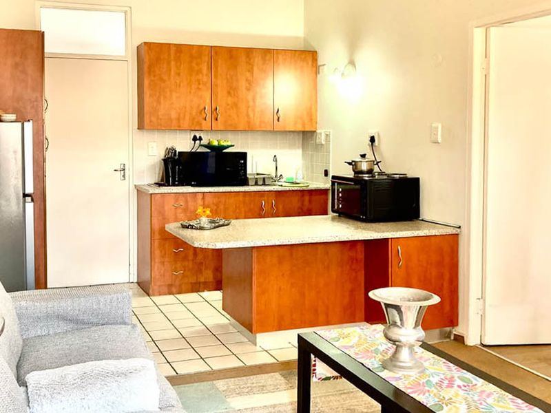 Open-plan living area featuring a compact kitchen with laminate cabinetry, stone-look countertops, and tiled flooring, providing a functional space for daily living.