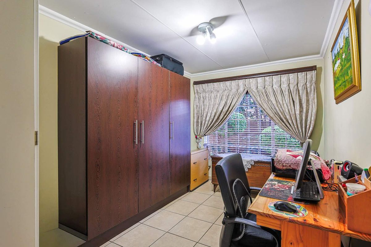 A functional bedroom featuring tiled flooring, built-in cabinetry, and a window with curtain treatments, suitable for use as a bedroom or home office.