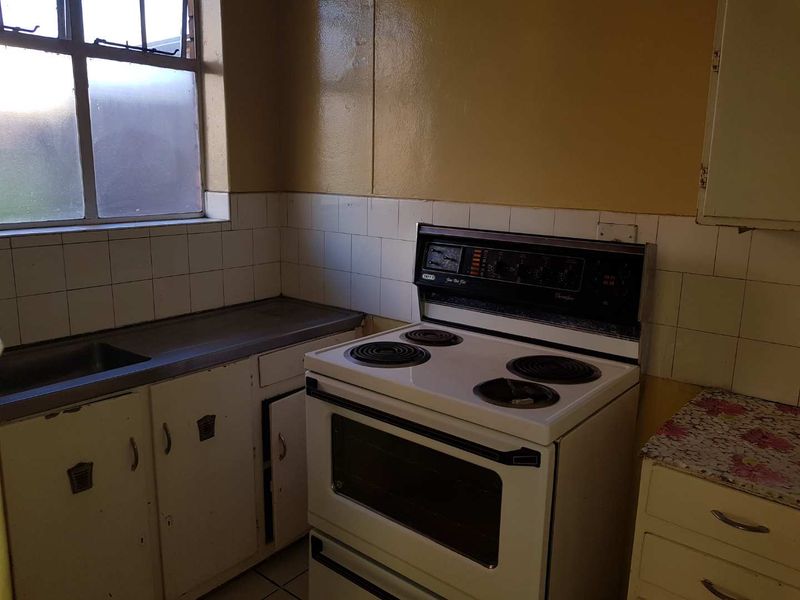 A dated kitchen featuring original cabinetry, a freestanding electric stove, and a stainless steel sink, requiring modernization to improve functionality and aesthetic appeal.