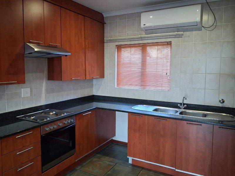 A functional kitchen featuring wood-finish cabinetry, granite countertops, integrated appliances, and a wall-mounted air conditioning unit.